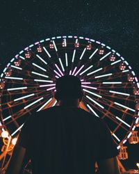 Rear view of silhouette man standing at illuminated amusement park