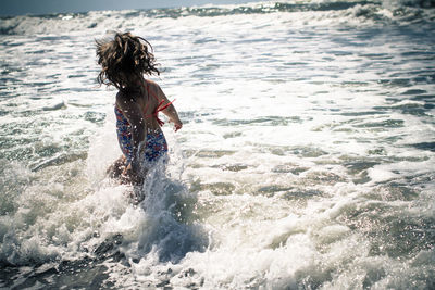 Girl running in water against sky during sunny day