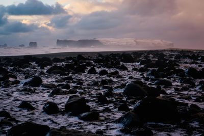 Rocks on beach against sky during sunset