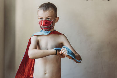 School age young boy dressed as super hero with face mask on at home