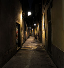 Rear view of woman walking on street amidst buildings at night