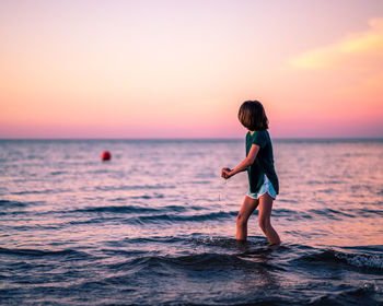 Full length of girl standing on beach against sky during sunset