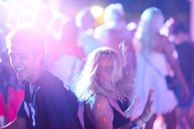 Cheerful friends dancing during music festival at night