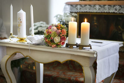 Illuminated candles with bouquet on table