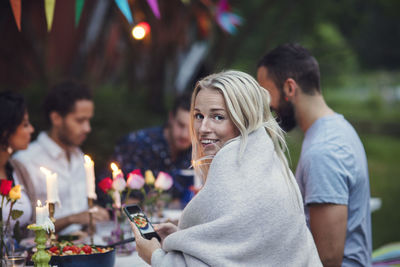 Portrait of smiling woman photographing food while sitting with friends at garden party