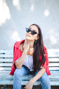 Portrait of beautiful young woman sitting on bench against wall