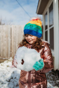 Young girl in rainbow hat holding giant snowball in winter