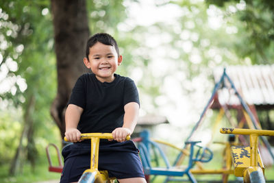 Portrait of smiling boy playing on seesaw at playground