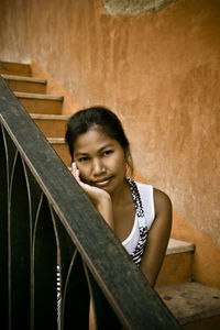 Young woman sitting on steps against orange wall