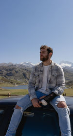 Man enjoys the environment in the mountains sitting on top of a car