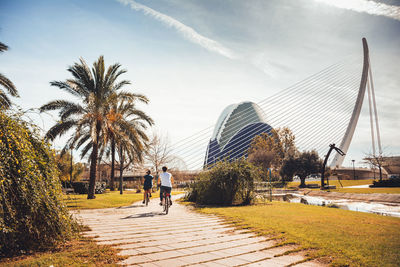 People walking on footpath by palm trees against sky