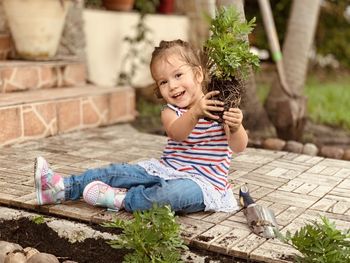 Smiling girl holding potter plant sitting outdoors