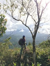 Side view of man standing by tree against sky