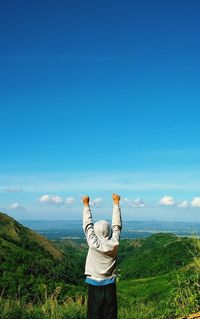 Rear view of person with arms raised standing against landscape