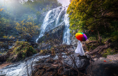 Asian female tourists  holding colorful umbrellas standing at khlong lan waterfalls in thailand