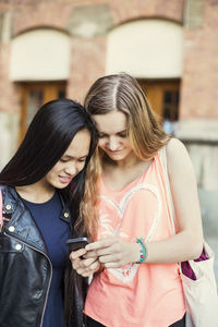 Female friends reading text message on smart phone at high school schoolyard