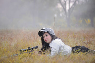 Young woman shooting rifle while lying on field