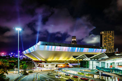 Illuminated street amidst buildings against sky at night