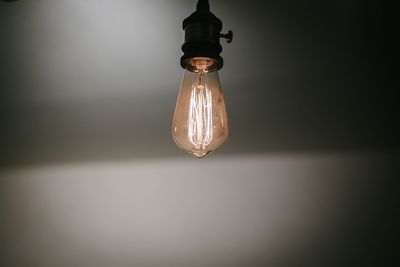 Close-up of illuminated light bulb hanging from ceiling