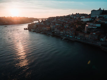 River amidst buildings in city against sky at sunset