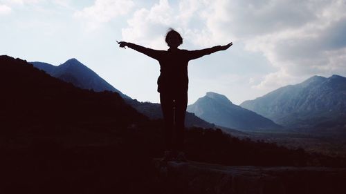 Man with arms outstretched standing on mountain against sky