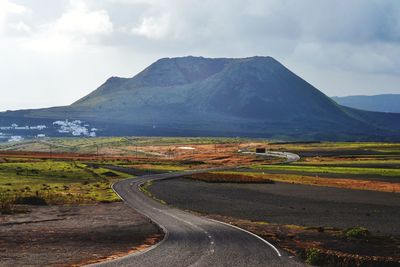 Empty road along landscape and mountains against sky