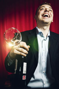 Close-up of man holding wineglass and bottle standing against curtain