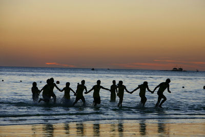 Silhouette children playing at sea shore against sky during sunset