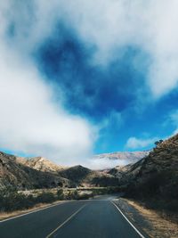 Diminishing perspective of road leading towards mountains against cloudy sky