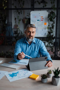 Senior business man working at tablet computer and looking at camera at contemporary office