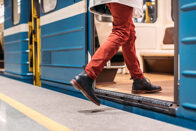 Handsome man in black shoes, burgundy pants and white jacket runs into a subway train. 