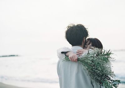 Rear view of couple kissing against sea