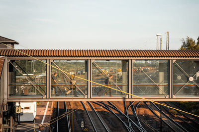 People walking on glass bridge over railroad tracks against clear sky