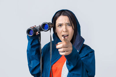 Portrait of young woman holding camera against white background