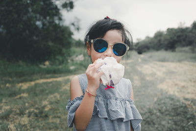 Portrait of woman holding sunglasses against plants