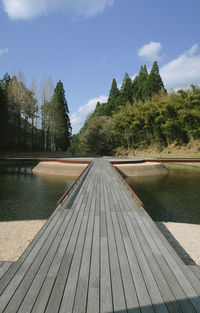 Wooden footbridge over lake against sky