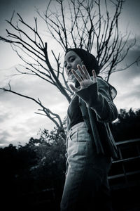 Portrait of young man standing by tree against sky