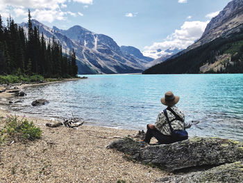 Rear view of man sitting on rock by lake