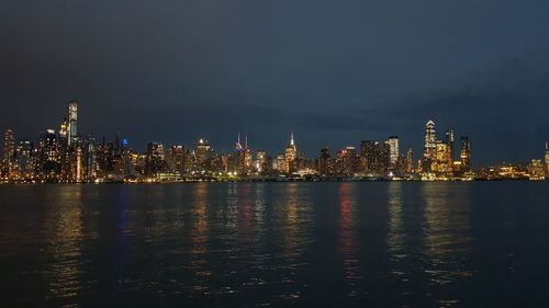 Illuminated buildings by river against sky at night