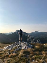 Rear view of man standing on rock against sky