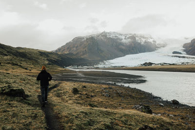 Rear view of man walking on landscape by lake against sky