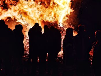 Silhouette of people standing against bonfire at night