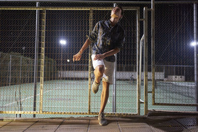 Young man standing against sports field at night