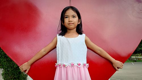 Portrait of young woman standing against red background wall