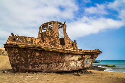 Old abandoned boat at beach against sky