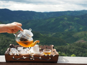 Midsection of person holding ice cream on table against mountains