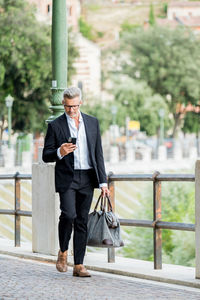 Businessman using mobile phone walking in city street and commut to work texting on smartphone. 