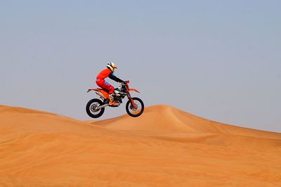 Man riding bicycle on desert against clear sky