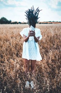 Woman covering face with plants while standing on field