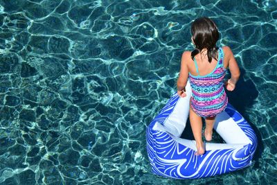 High angle view girl standing on inflatable ring in swimming pool